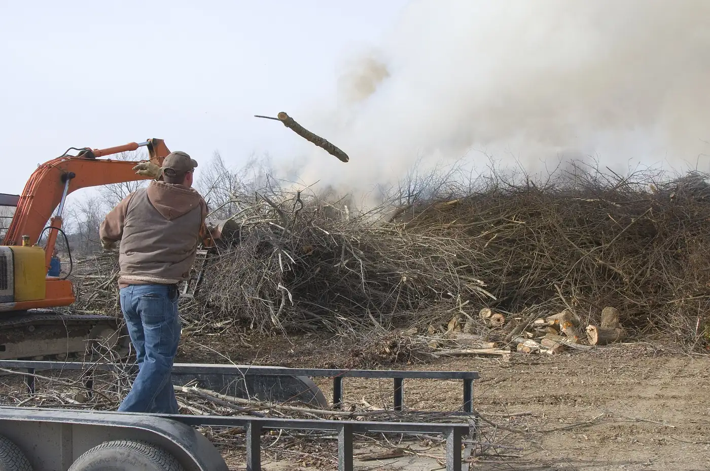 Worker and excavator clearing a storm debris pile